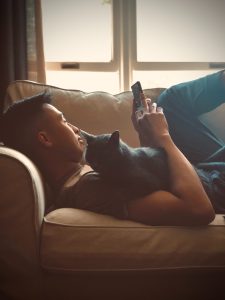 Man laying on couch playing free internet sweepstakes games on phone.